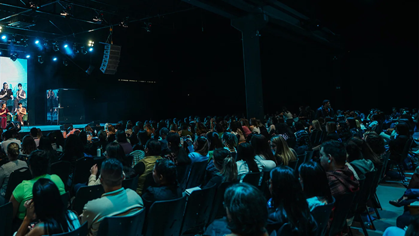 Auditório lotado durante uma apresentação, visto do meio da plateia