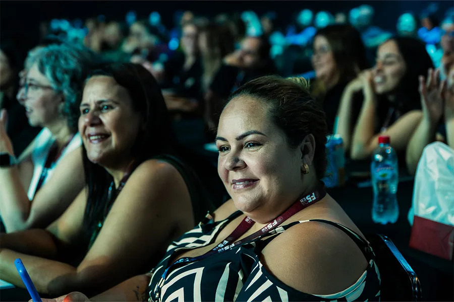 Participantes sorrindo na plateia enquanto acompanham uma palestra